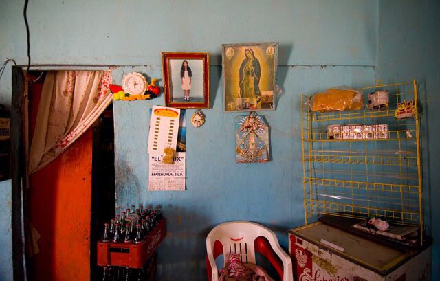 Stol i et rom med bilder på vegge, jomfru maria og cola-kasse.