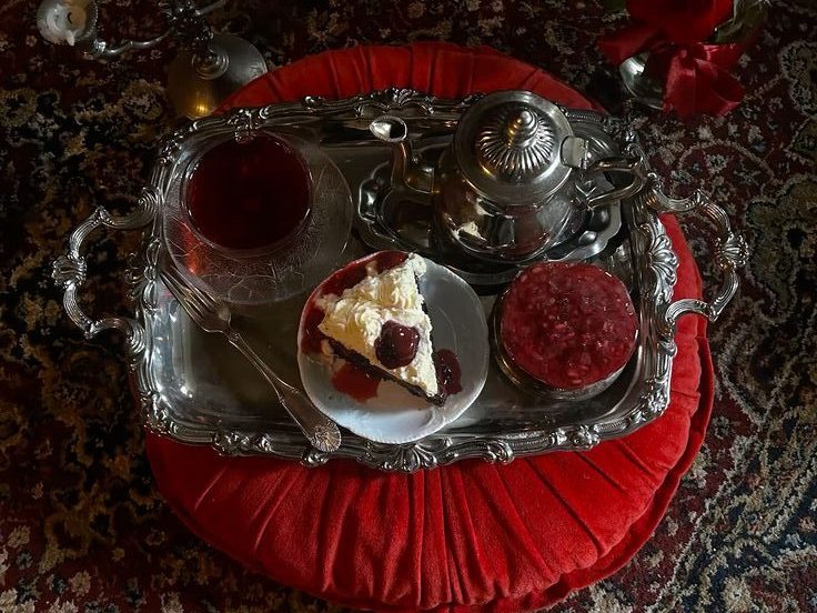 Sølvbrett med te, kake, syltetøy og sølvgaffel på en rød pute oppå et persisk teppe.