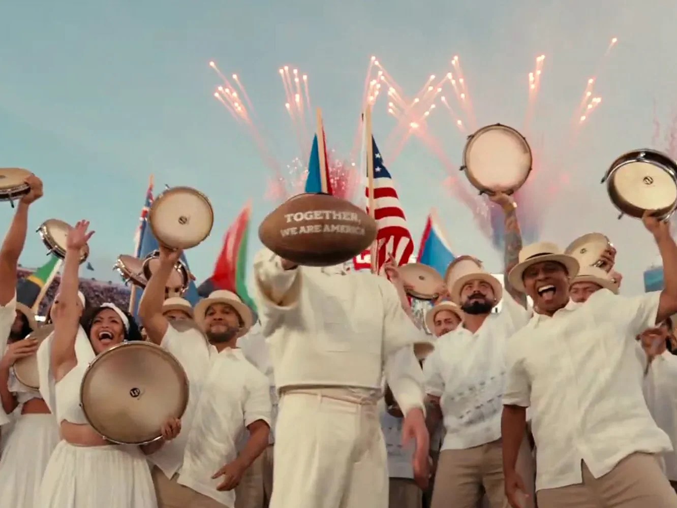 Bad Bunny viser ball med teksten together we are america. Fyrverkeri i bakgrunn, og mennesker med instrumenter.