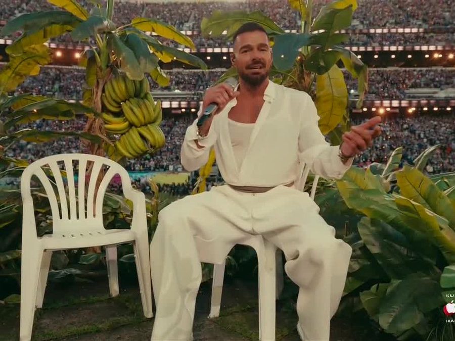 Ricky Martin på plast stol med mikrofon, banantrær i bakgrunn.